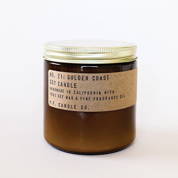 Candle features amber glass with a gold lid. The label is kraft paper with typewriter font that reads "No.21: Golden Coast Soy Candle Handmade in California with 100% Soy Wax. P.F. Candle Co."