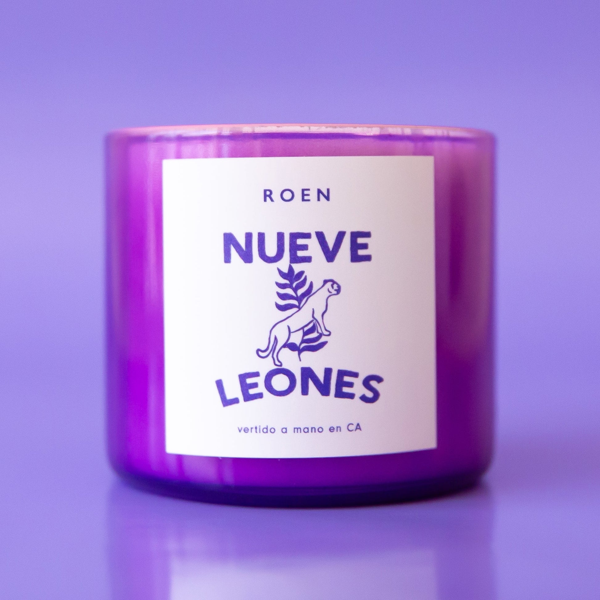 A purple glass candle with a white label with, "Nueve Leones".