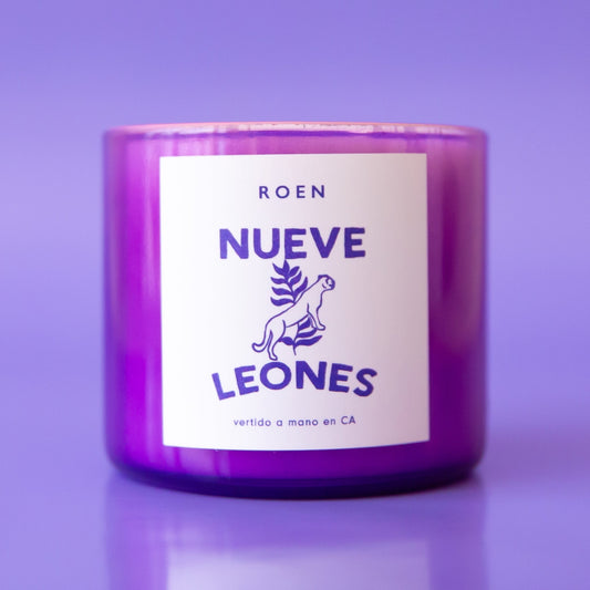 A purple glass candle with a white label with, "Nueve Leones".