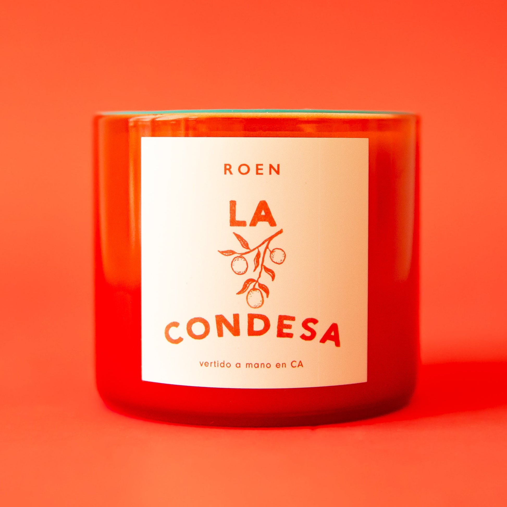 An orange/red glass jar candle with a label that reads, "La Condesa".
