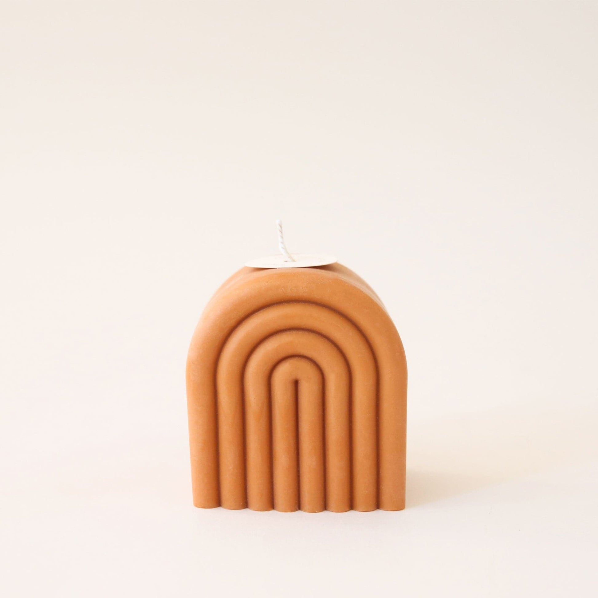 Single short, arch shaped candle. The candle is carved with rainbow-shaped curves and has a white wick sprouting from the top.
