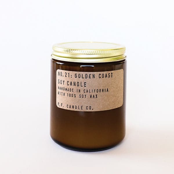 Candle features amber glass with a gold lid. The label is kraft paper with typewriter font that reads "No.21: Golden Coast Soy Candle Handmade in California with 100% Soy Wax. P.F. Candle Co."
