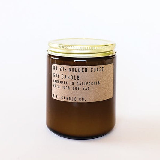 Candle features amber glass with a gold lid. The label is kraft paper with typewriter font that reads "No.21: Golden Coast Soy Candle Handmade in California with 100% Soy Wax. P.F. Candle Co."